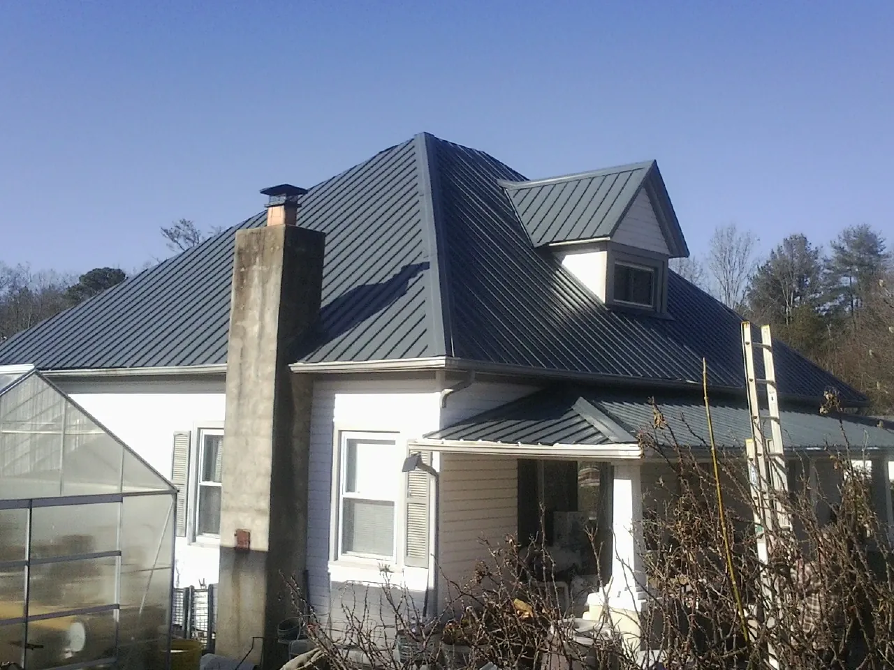 Dark blue standing seam metal roof on a white farmhouse with dormer — Slate & Tile Roof Repair by Roofing Brothers in Amherst