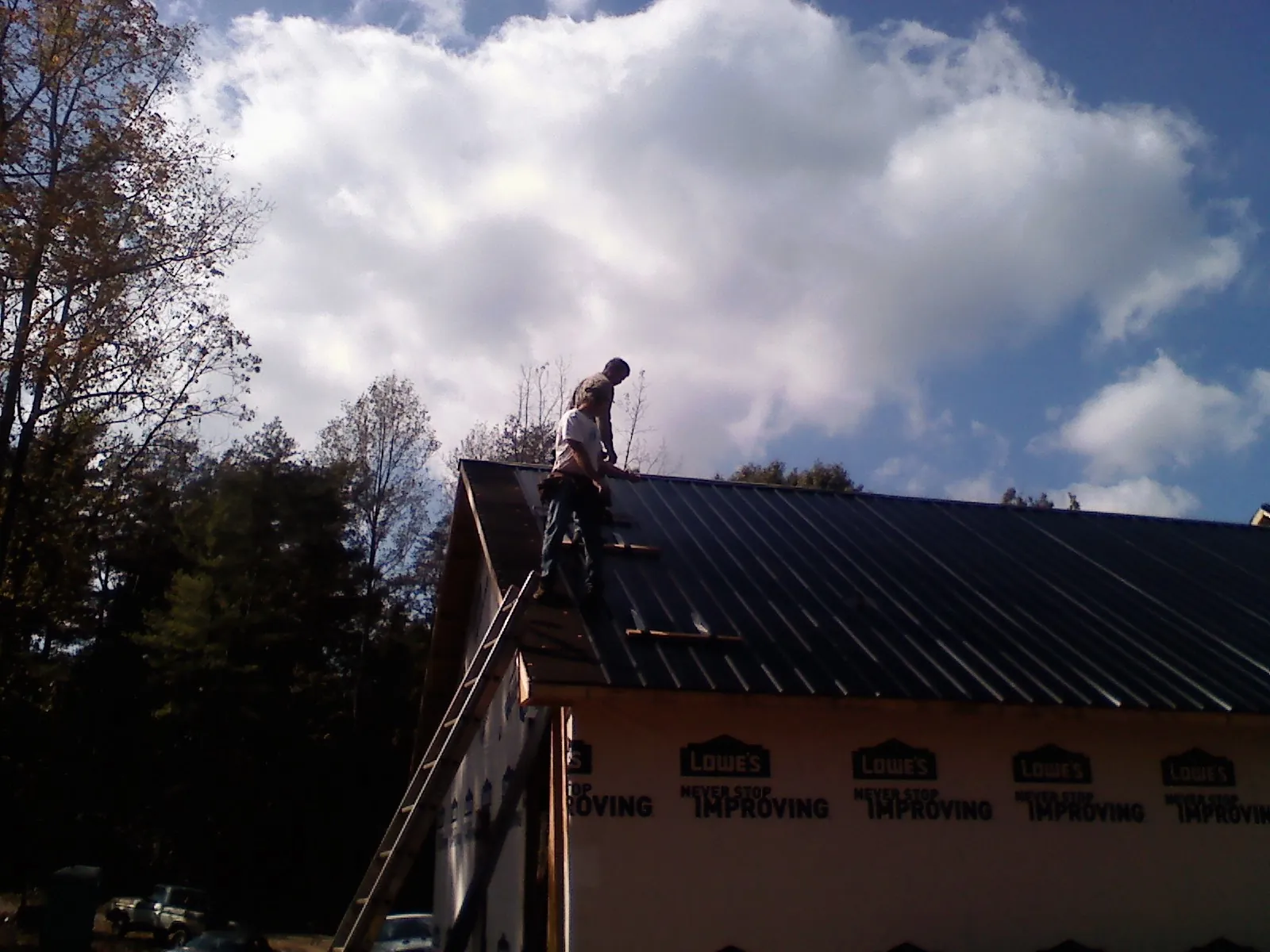 Roofer fastening dark metal panels high against a cloudy sky, from a Roof Inspection job in Amherst